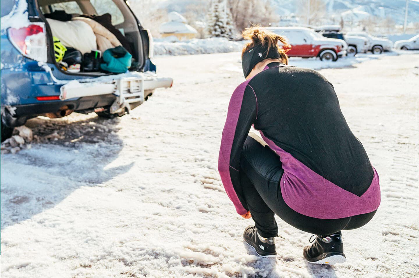 Man putting snow pants over his base layer with car trunk open